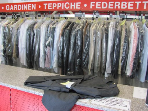 Abgelegte schwarze Anzüge hängen auf einer Kleiderstange, darunter liegt eine schwarze Hose.